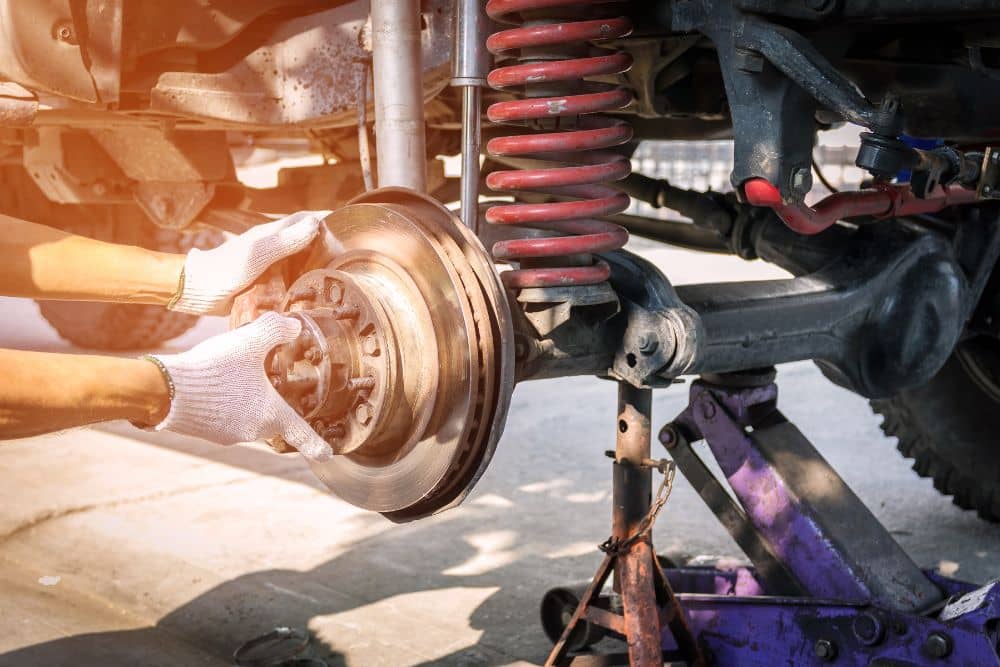 Hands performing suspension repair on a vehicle, focusing on the brake rotor and strut assembly, highlighting essential auto maintenance for a smooth ride.