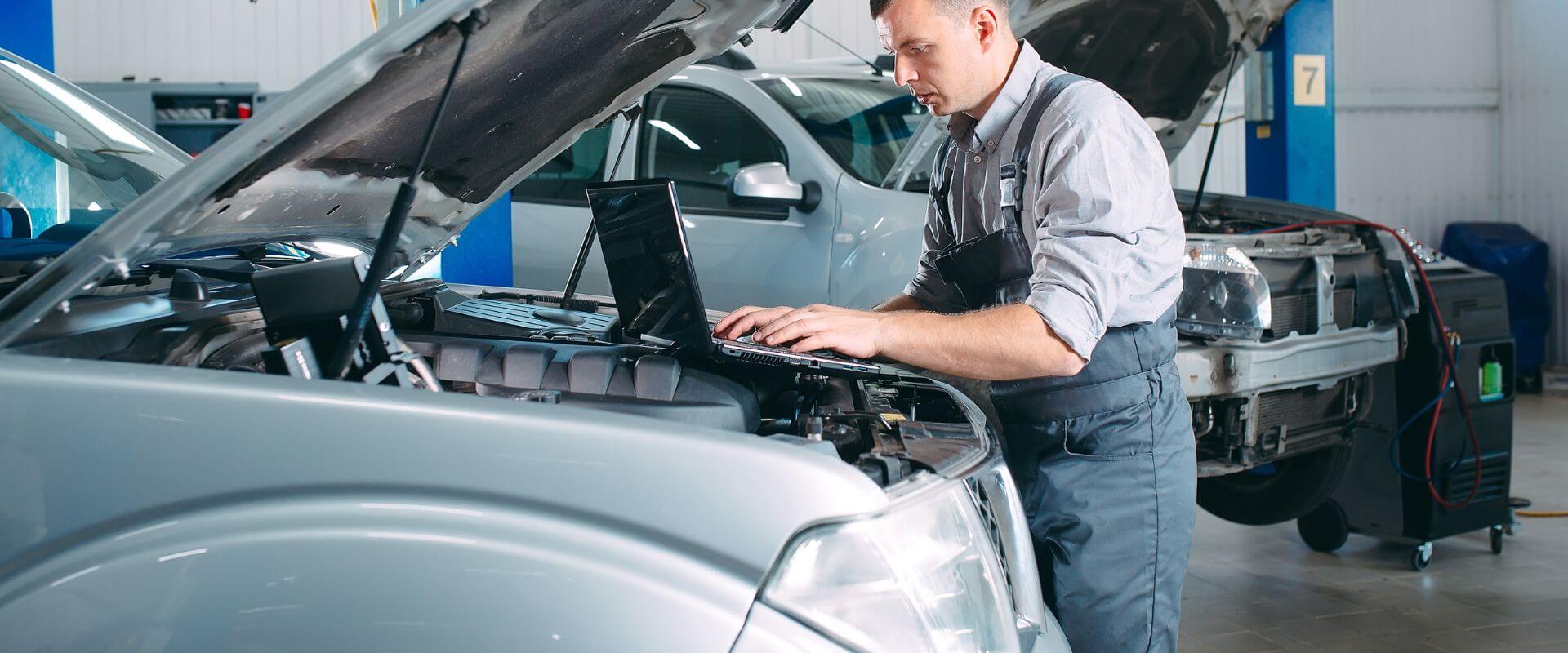 Mechanic using laptop for auto diagnostics on vehicle in repair shop, emphasizing vehicle maintenance and repair services at Asher Auto Care in Dallas, TX.