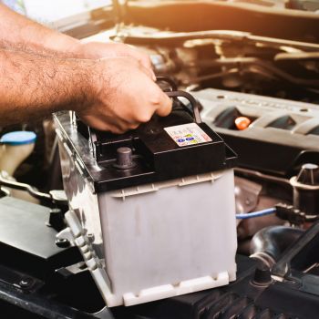 Person installing a car battery under the hood, highlighting battery maintenance and repair services at Asher Auto Care in Dallas, TX.