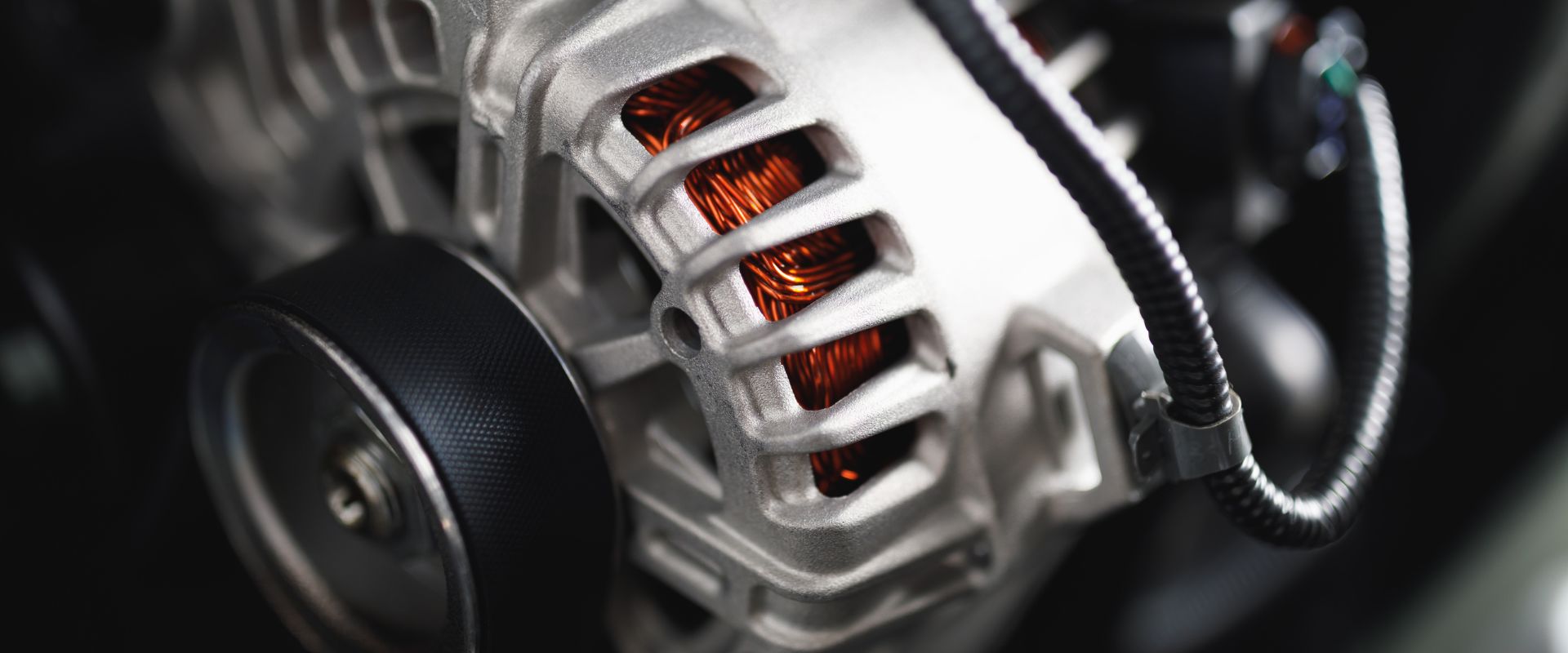 Close-up of an alternator showcasing copper windings and a black pulley, illustrating key components of vehicle electrical systems for battery, starter, and alternator repair services in Dallas, TX.