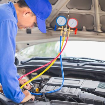 Mechanic performing AC repair using diagnostic gauges on a car engine in a service setting.