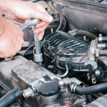 Mechanic using a wrench to repair an engine, highlighting the importance of immediate car maintenance and professional inspection at Asher Auto Care in Dallas, TX.
