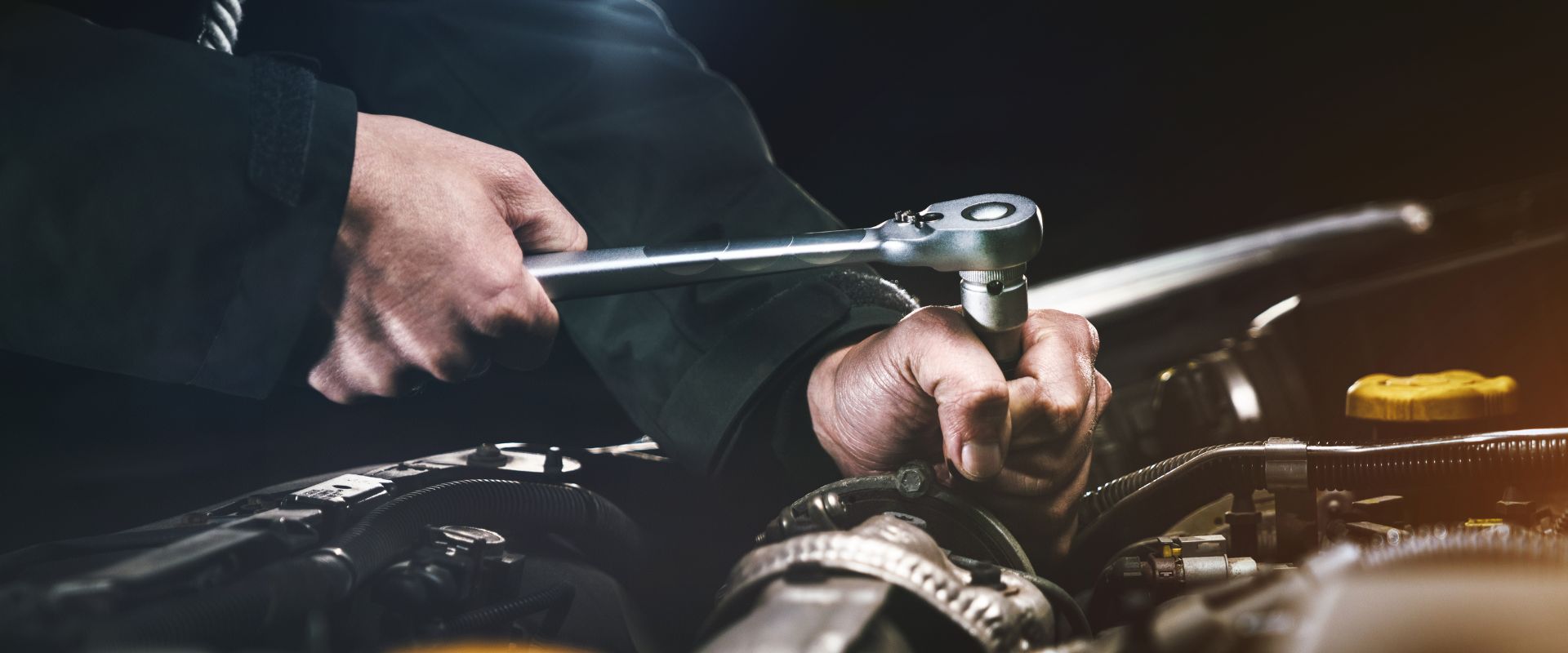 Mechanic using a ratchet wrench to perform car repair work under the hood, highlighting automotive maintenance services at Asher Auto Care in Dallas, TX.