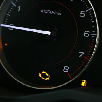 Check engine light and fuel warning indicator illuminated on a car dashboard gauge.