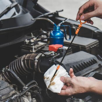 Person checking oil level with dipstick in car engine, emphasizing automotive maintenance services at Asher Auto Care in Dallas, TX.